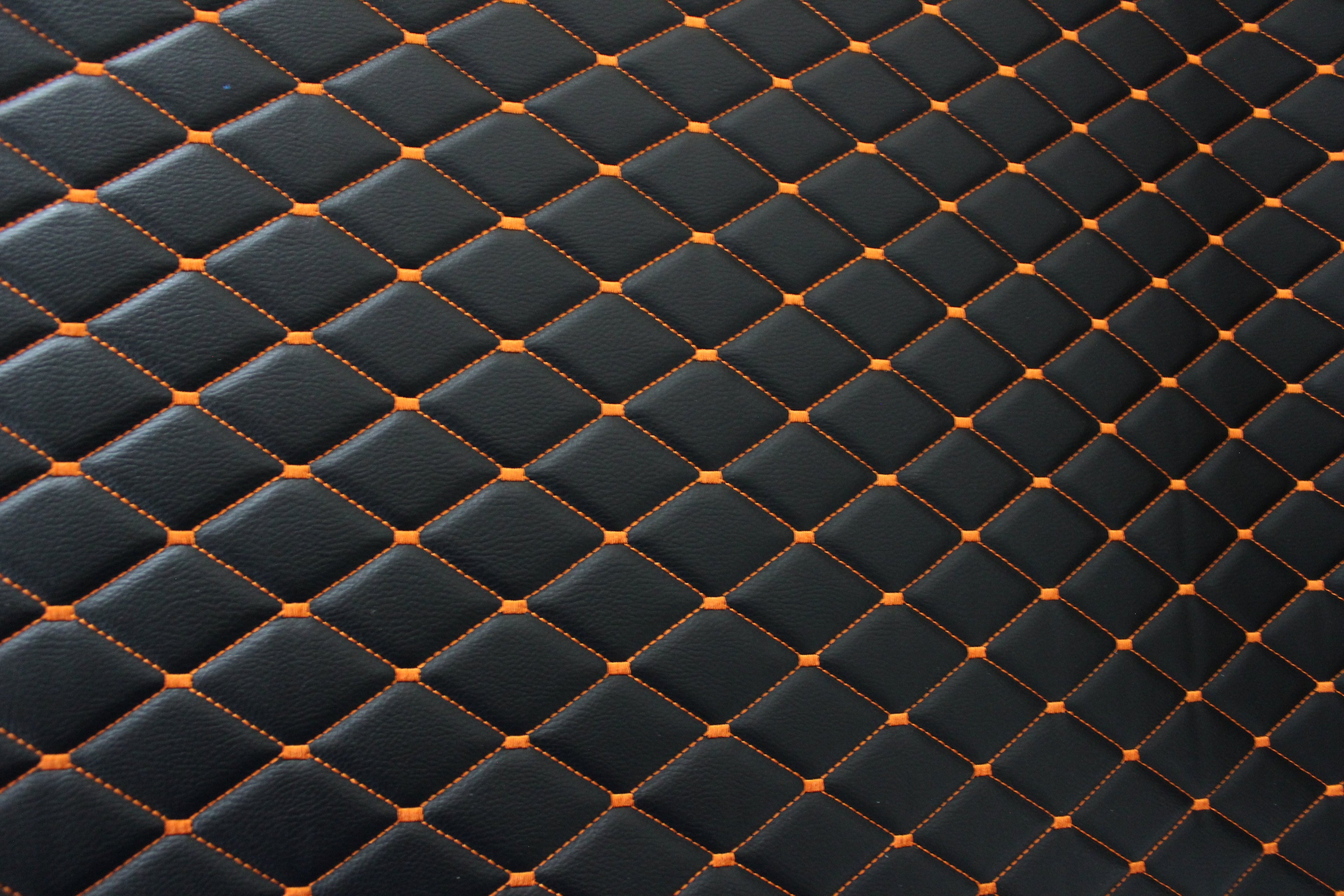 Tecido para estofos automóveis em vinil preto acolchoado laranja com textura granulada | Costura em losango de 5x8cm com espuma | 140cm e 55,1" de largura | Pele sintética (réplica)